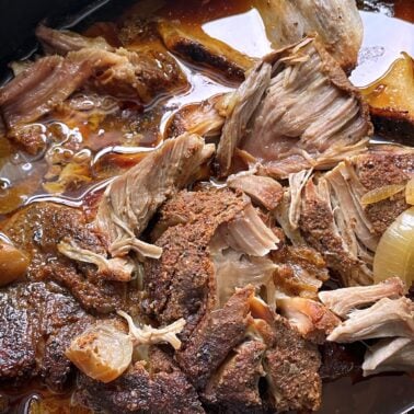 Close-up of tender, slow-cooked pork with a crispy crust and onions in a rich sauce.