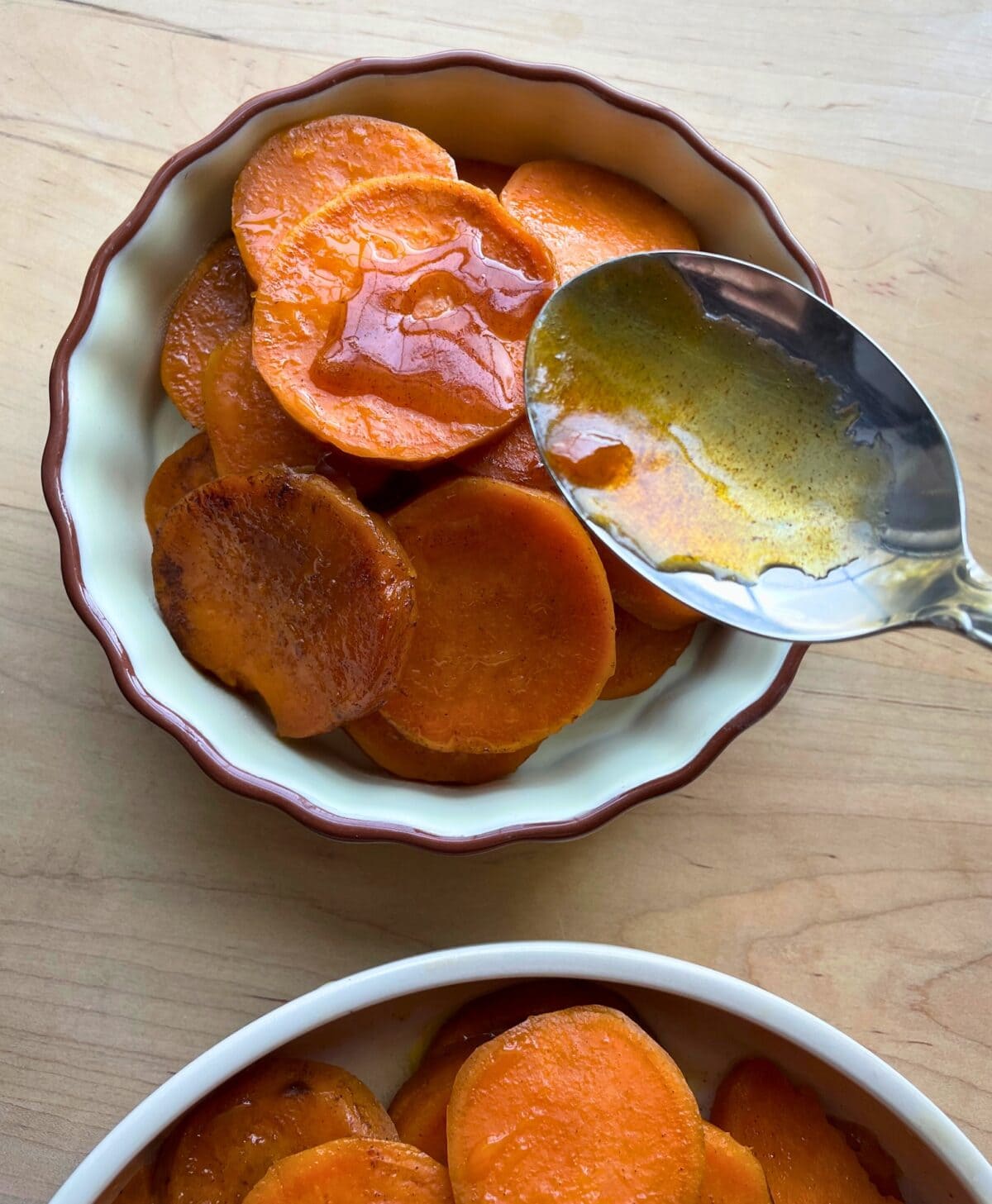 A bowl of glazed candied sweet potatoes with a spoon, served on a wooden table.