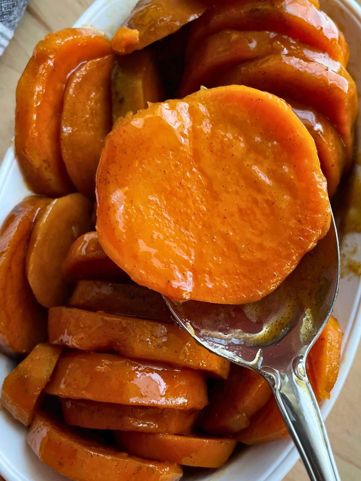 A close-up view of glazed candied sweet potatoes in a dish with a spoon.