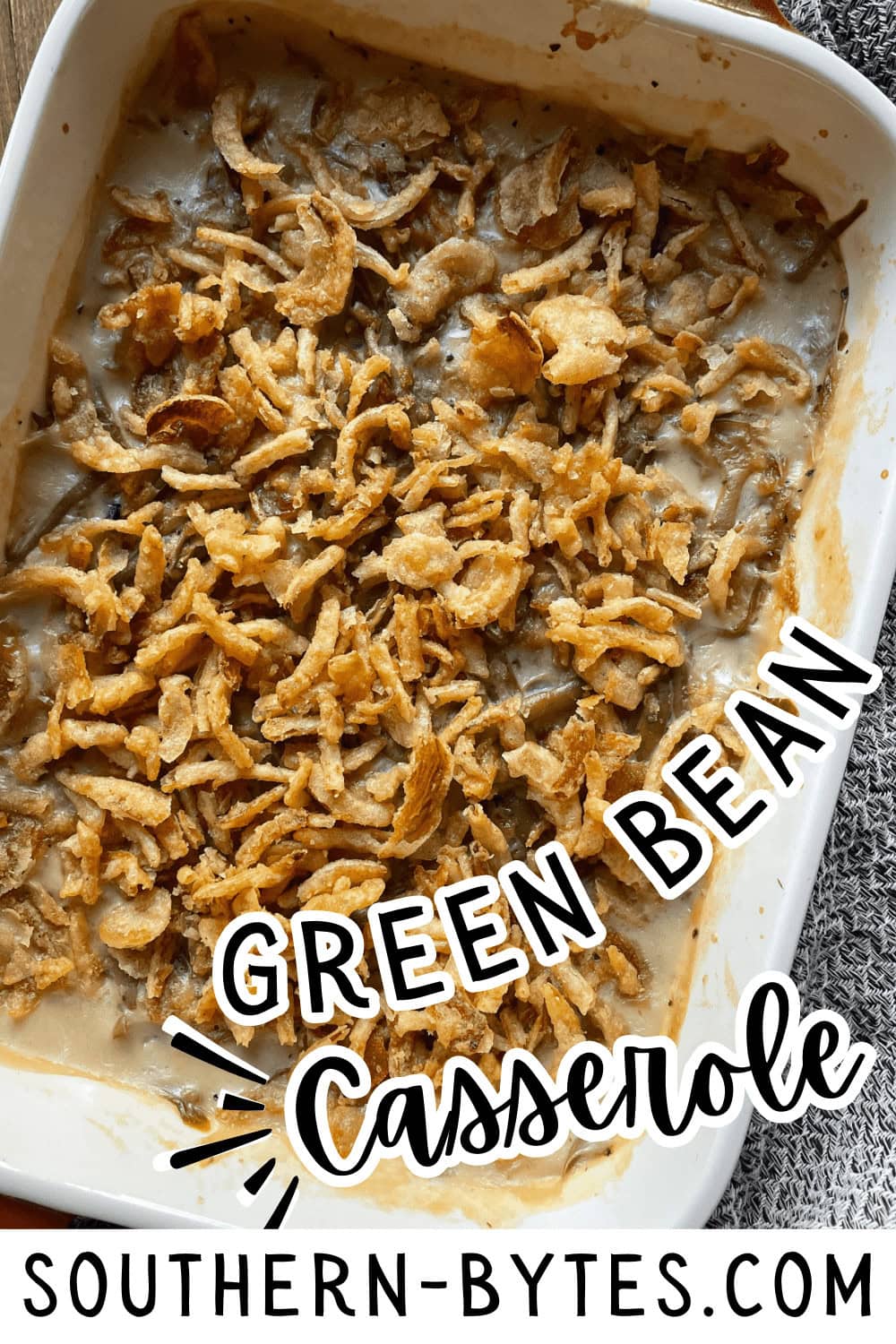 A pin image of a casserole dish of green bean casserole made with cream of mushroom soup, french cut green beans, and topped with crispy fried onions.