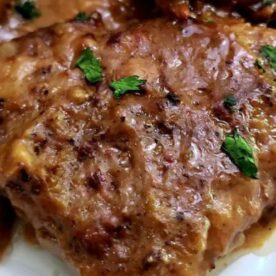 Close-up of a cube steak topped with brown sauce and garnished with parsley on a white plate.