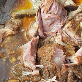 Close-up of tender slow-cooked pork with onions in broth, showcasing the succulent textures and rich colors.