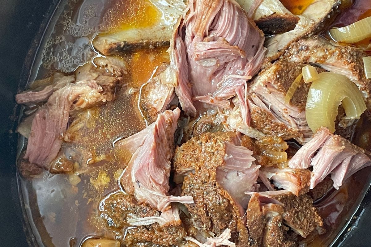 Close-up of tender slow-cooked pork with onions in broth, showcasing the succulent textures and rich colors.