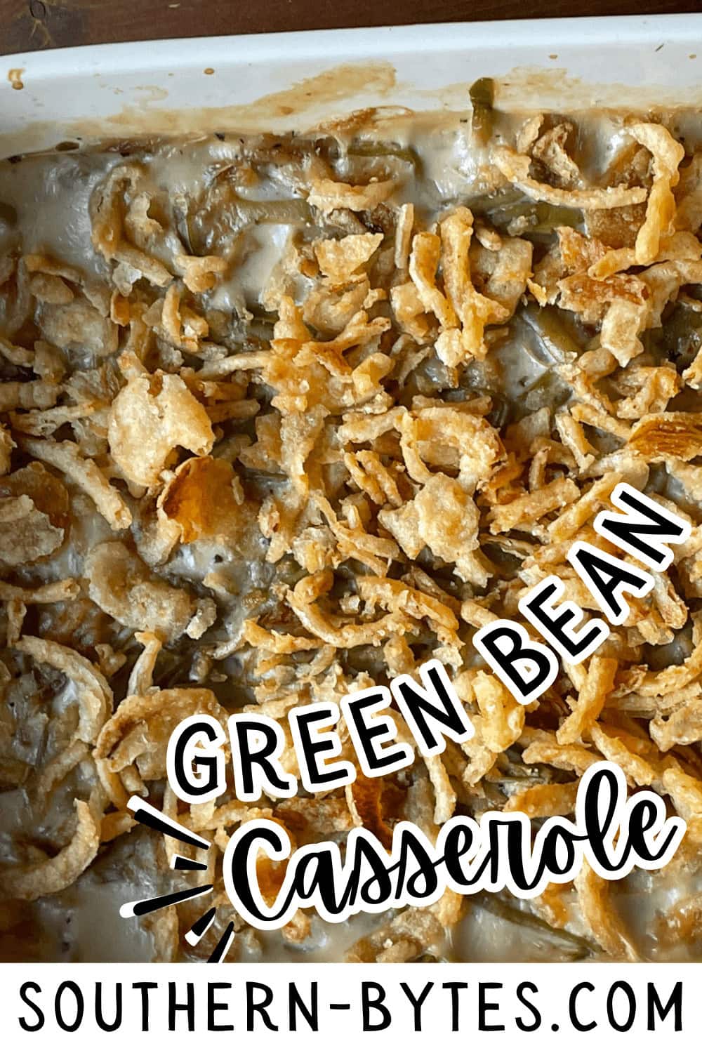 A pin image of a baking dish filled with green bean casserole topped with crispy fried onions.