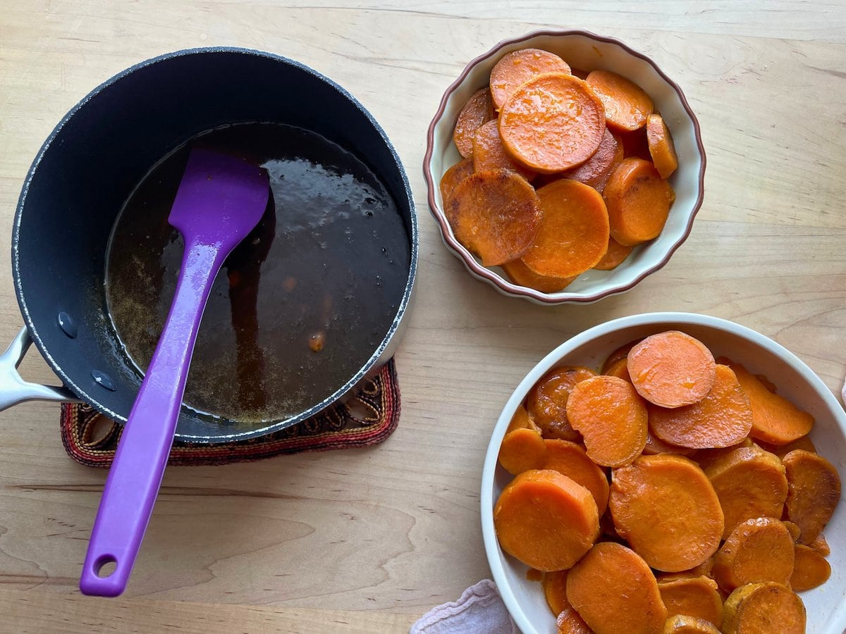 Two bowls of sliced sweet potatoes and a saucepan of brown sugar glaze.