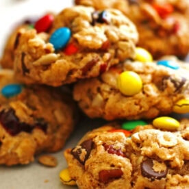 Close-up of homemade cookies with mixed candies, nuts, and chocolate chunks on a light surface.