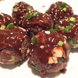 A plate of glazed meatballs topped with sesame seeds and chopped green onions.