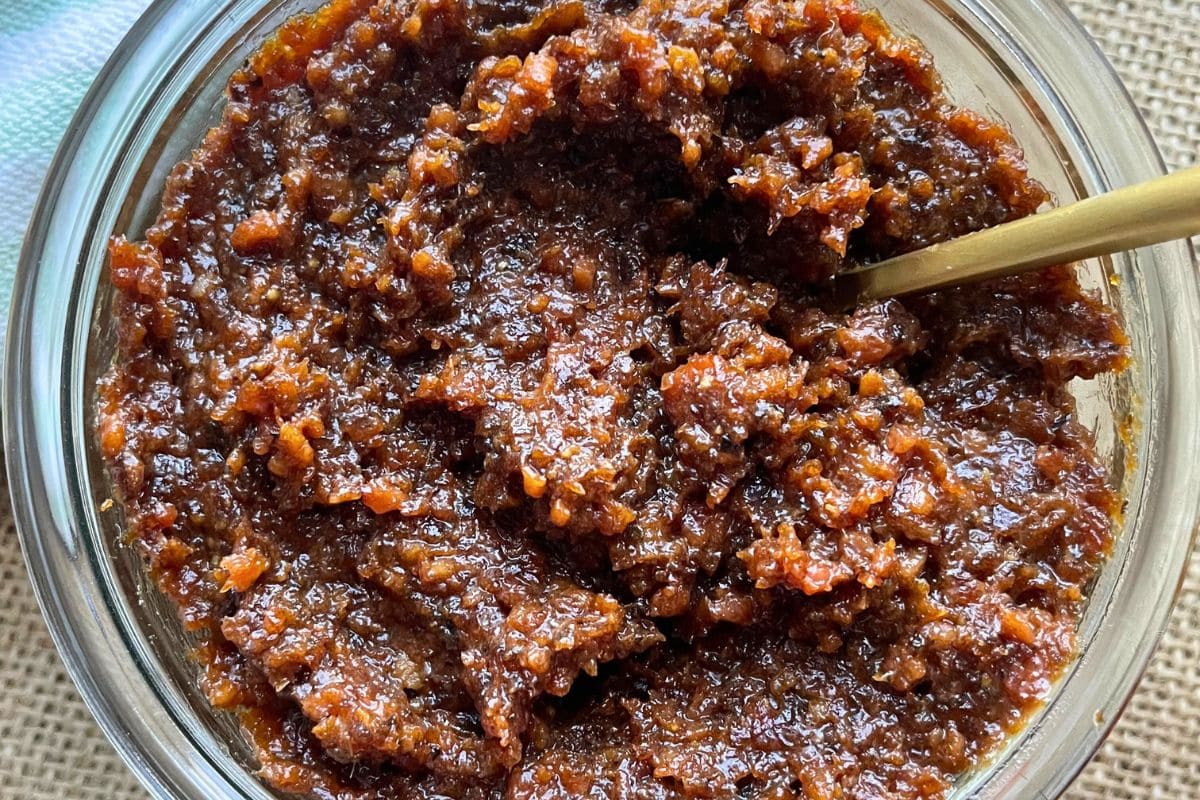 A glass jar filled with bacon jam with a spoon inside it.