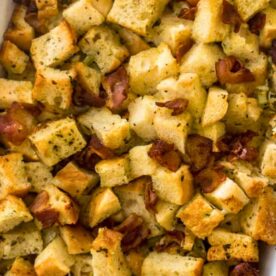 A dish of homemade bread stuffing with herbs and crispy edges in a white baking dish.