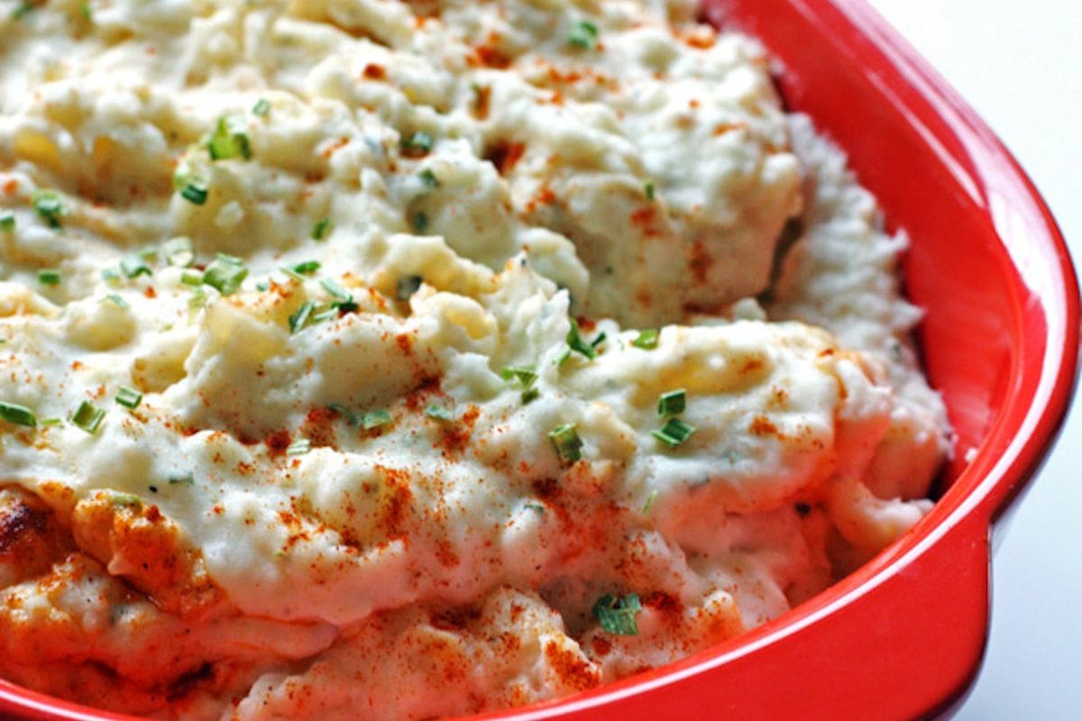 A bowl of fluffy mashed potatoes topped with chives and paprika in a vibrant red serving dish.