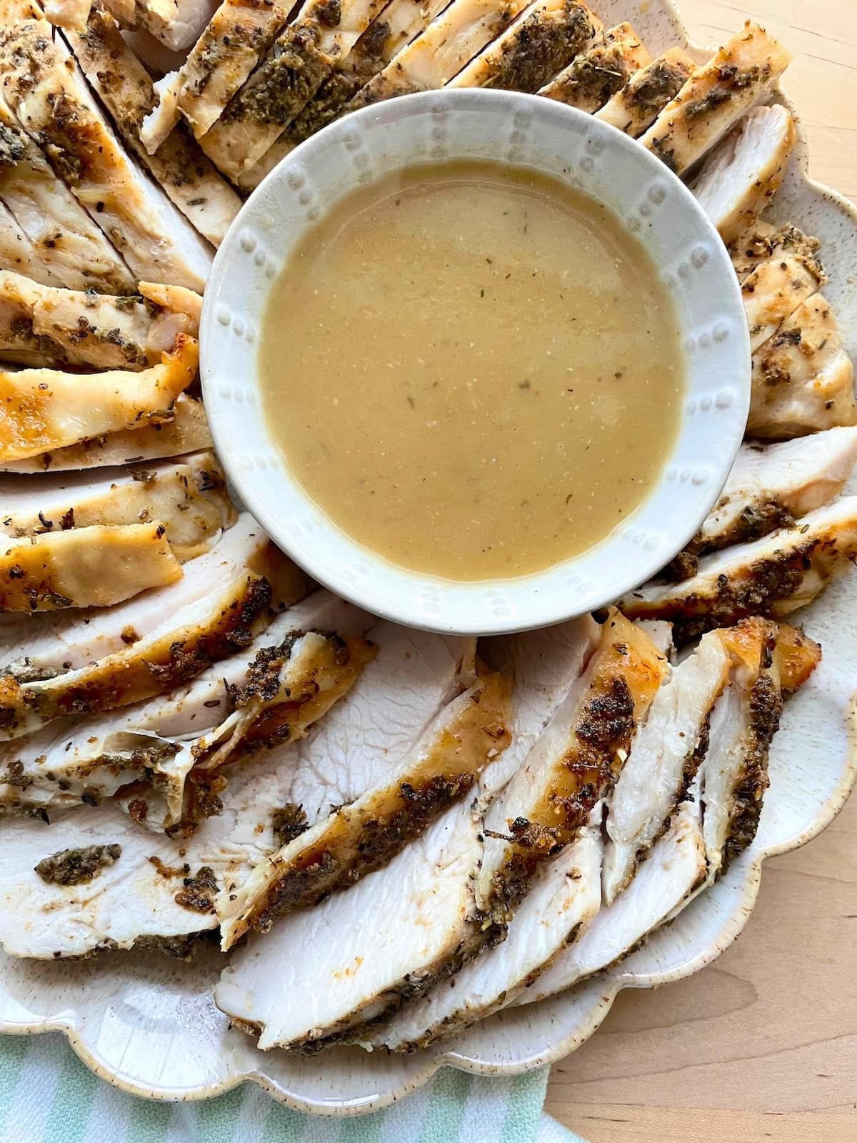 Sliced, seasoned turkey breast arranged on a platter with a bowl of gravy in the center.