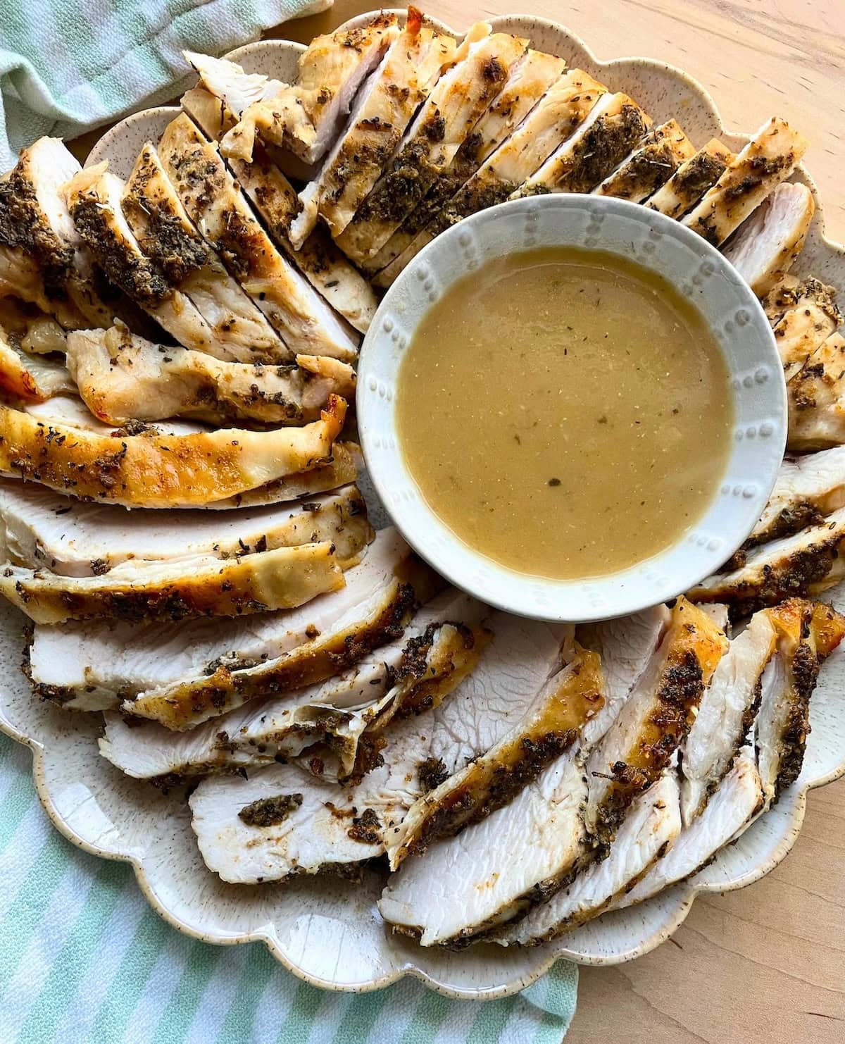 A plate of herb-crusted turkey breast, thinly sliced and served with a side of gravy.