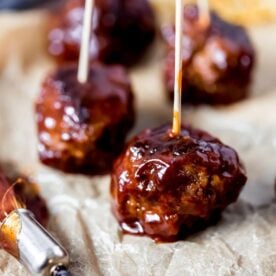 Close-up of glazed barbecue meatballs skewered with toothpicks on parchment paper.