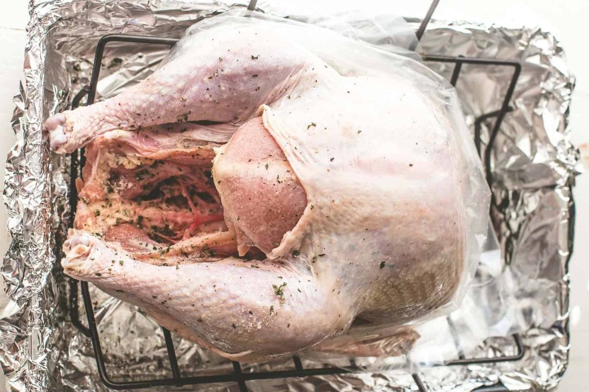 A raw turkey seasoned with herbs on a roasting rack, prepared for cooking.