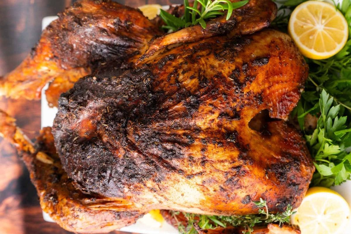 A whole roasted turkey with crispy skin garnished with parsley and lemon slices on a wooden table.