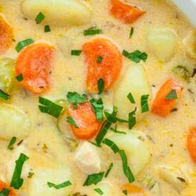 Close-up of a bowl of creamy vegetable soup garnished with fresh herbs, featuring carrots, potatoes, and celery.