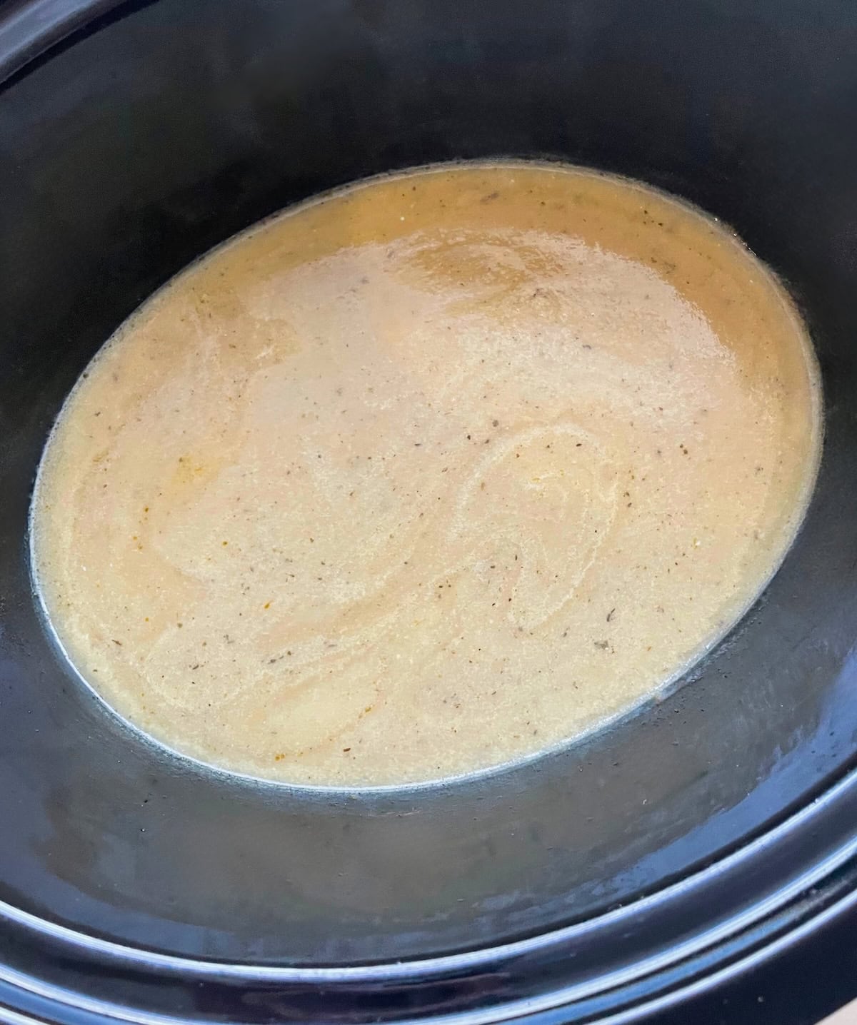 A close-up view of a turkey gravy simmering inside a black crock pot.