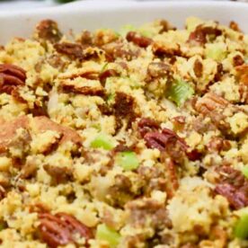 Close-up of homemade cornbread stuffing with pecans and green celery in a baking dish.