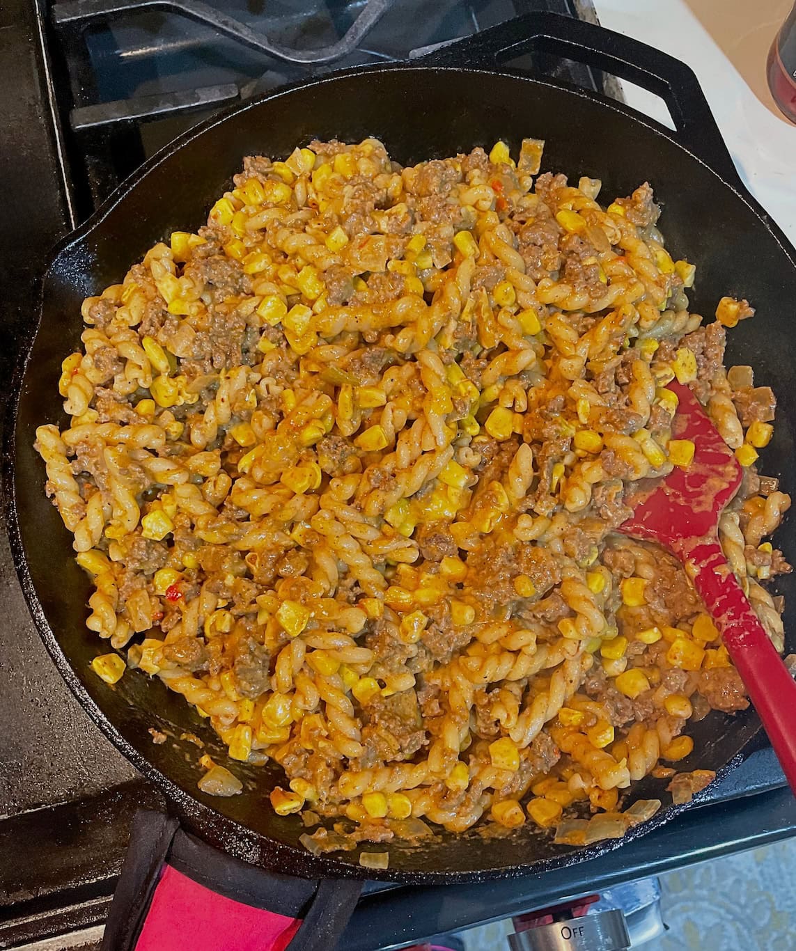 A close-up view of a savory skillet dish with ground beef, corn, and taco pasta being cooked on a stovetop.