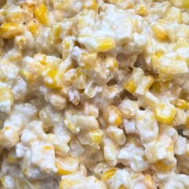 Close-up image of a creamy corn casserole with visible kernels and a spoon.