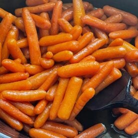 A close-up view of shiny glazed baby carrots in a black cooking pot with a black spatula.