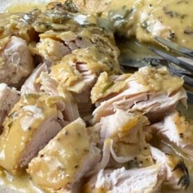 A close-up of sliced turkey tenderloin topped with a creamy herb sauce on a plate with a fork.