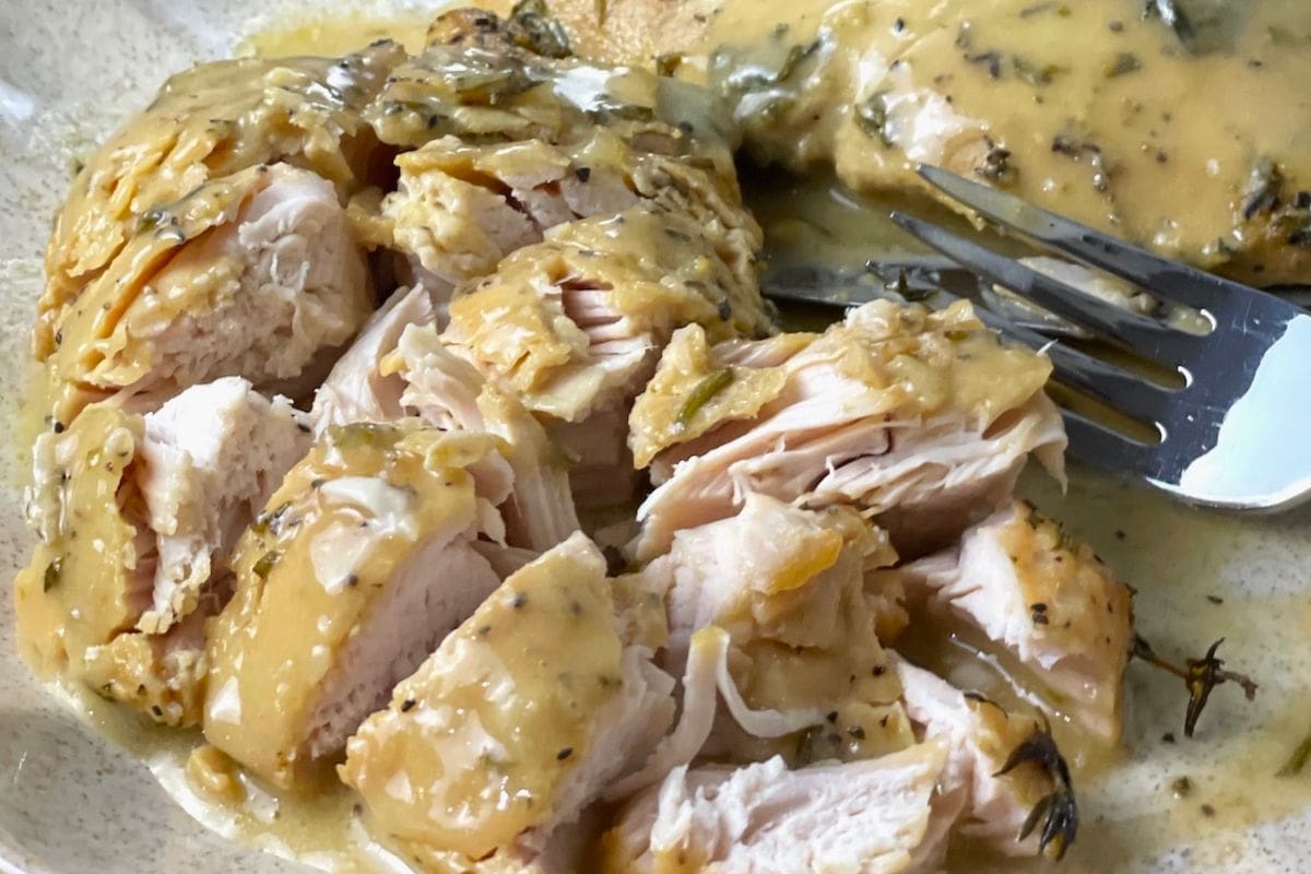 A close-up of sliced chicken breast topped with a creamy herb sauce on a plate with a fork.