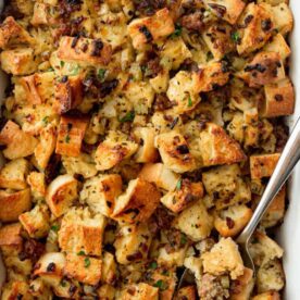 Close-up of homemade sausage stuffing in a baking dish, with toasted bread cubes and herbs.