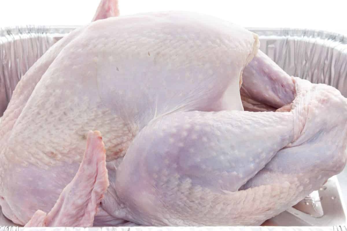 A raw, plucked turkey without giblets, positioned in a disposable aluminum roasting pan, ready for seasoning or stuffing before cooking.