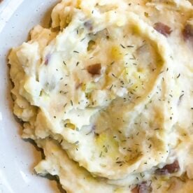 A close-up of homemade mashed potatoes garnished with herbs on a white plate.