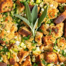 A close-up image of savory herb stuffing with chunks of toasted bread, diced celery, herbs, and sage leaves.