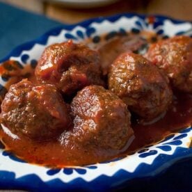 Close-up image of five meatballs covered in tomato sauce, served on a decorative blue and white ceramic plate.