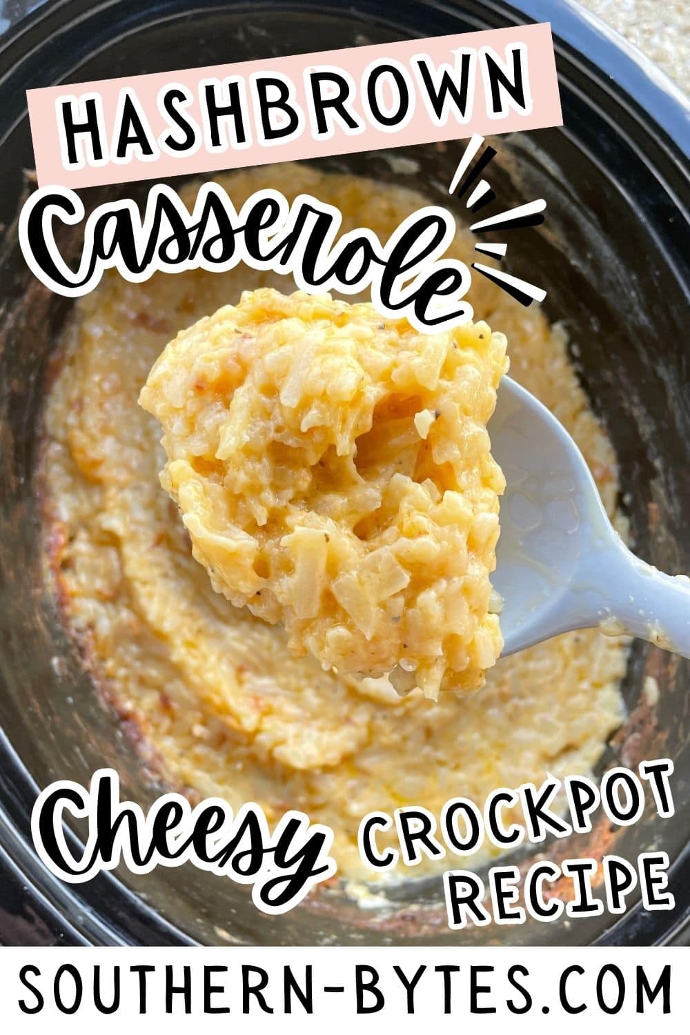 A pin image of a spoon lifting a serving of cheesy hashbrown casserole from a crockpot.