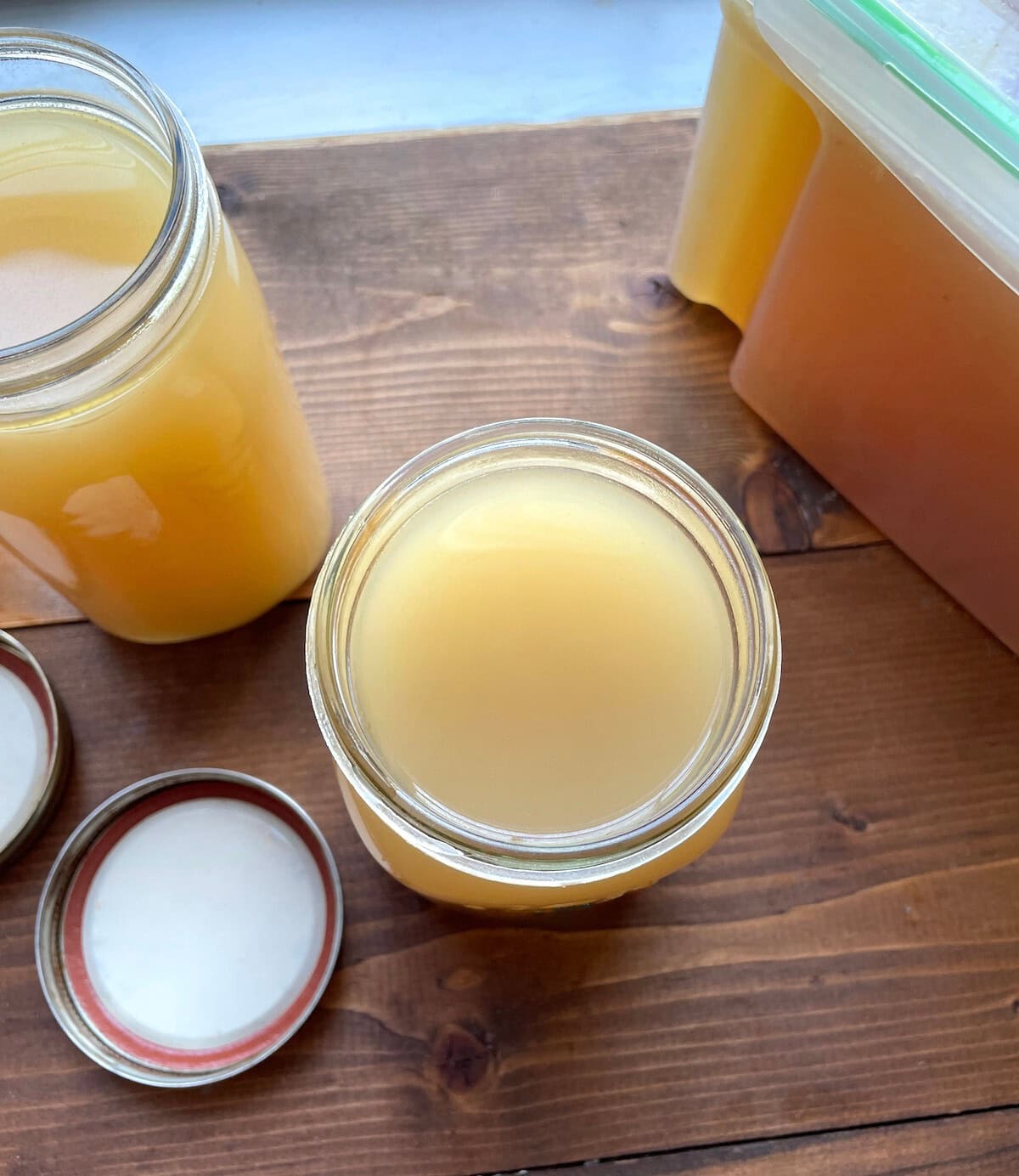 A top view of homemade pressure cooker turkey broth in various jars on a wooden surface.