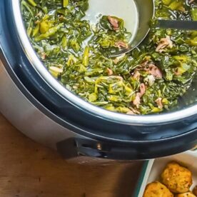 A pot of cooked greens with bits of meat on a wooden surface, next to a bowl of seasoned dough balls.