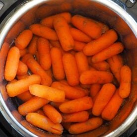 A heap of whole carrots inside a stainless steel pressure cooker.