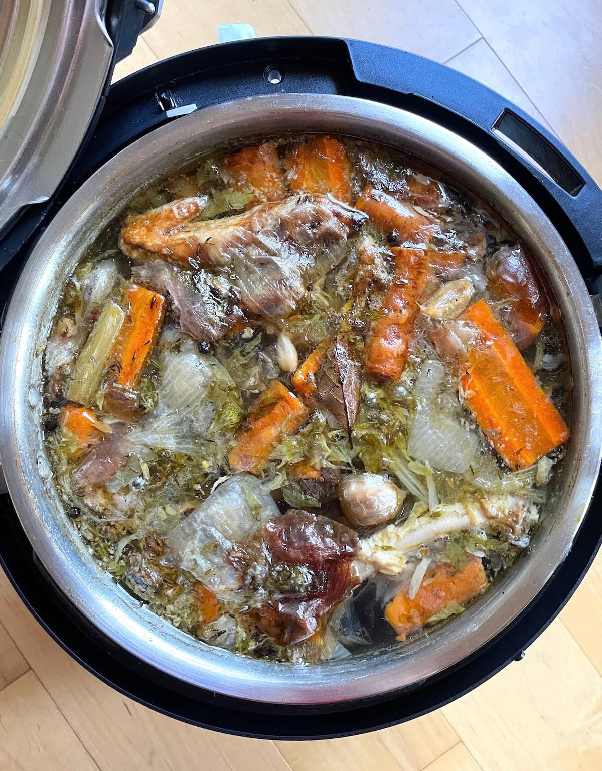 Top-down view of a pressure cooked stock with turkey wings, carrots, celery, and onions inside an open pressure cooker after cooking.