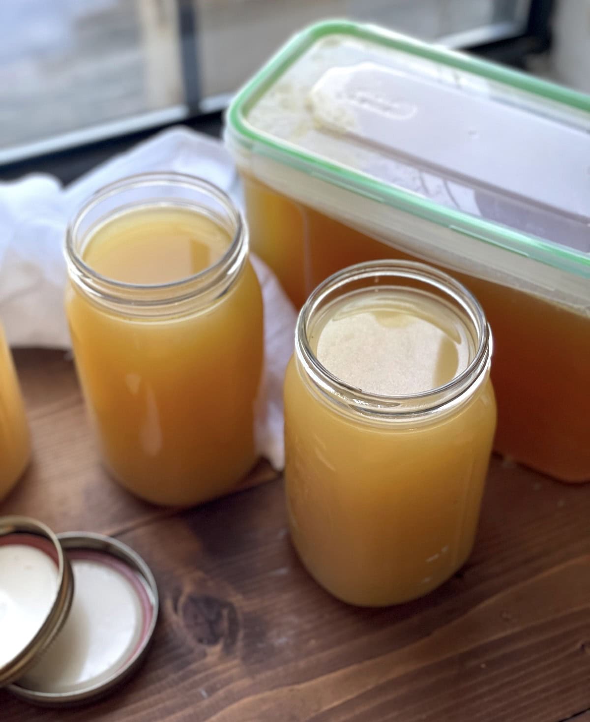 Several jars filled with homemade instant pot turkey broth on a wooden table, with one container with a green lid in the background.