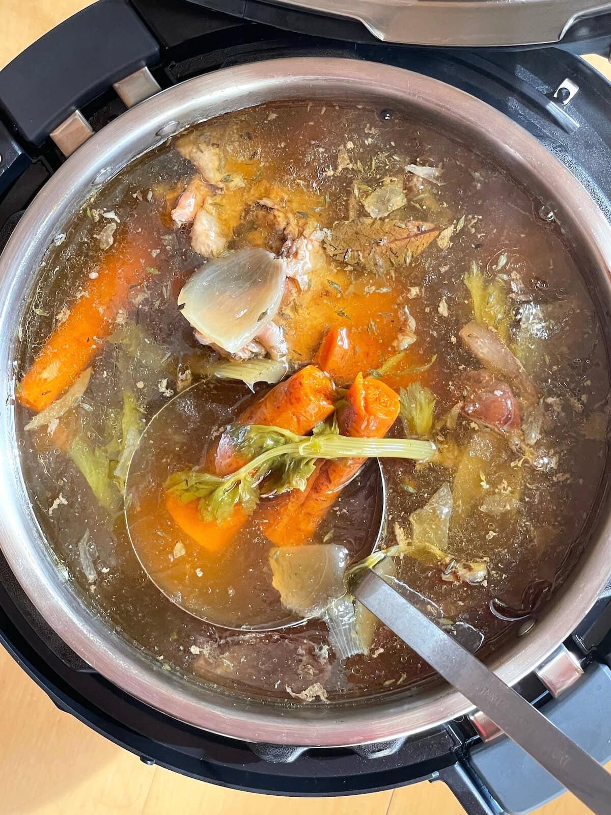 A pot of homemade broth in an Instant Pot with turkey bones, celery, onions, carrots, and herbs.