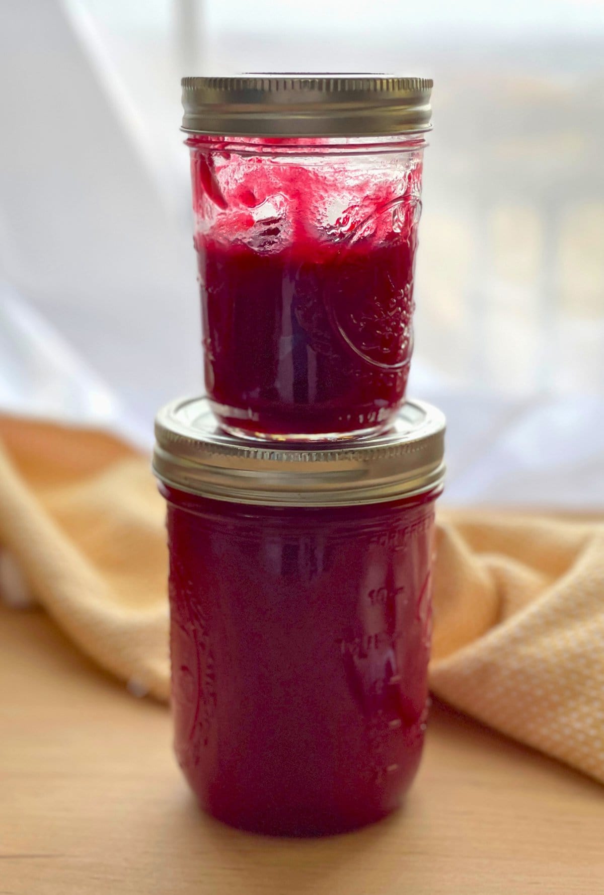 Two sealed glass jars stacked with homemade cranberry sauce against a blurred background.