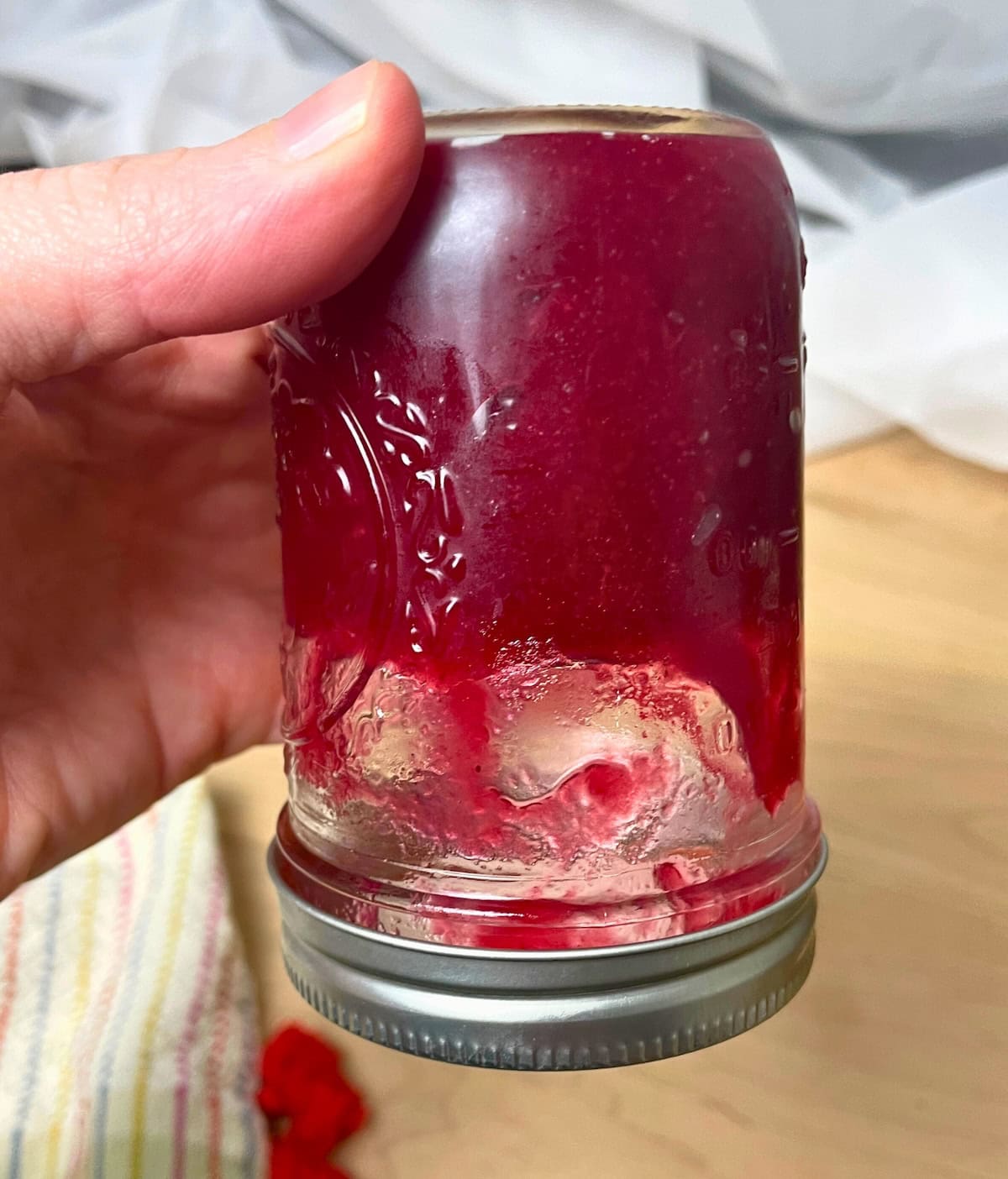 A close-up view of a person's hand holding an overturned cranberry sauce jar showing that it is so thick it holds it's shape.