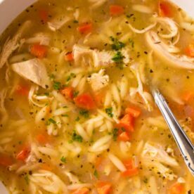 A bowl of chicken noodle soup with shredded chicken, noodles, carrots, and parsley garnish viewed from above.