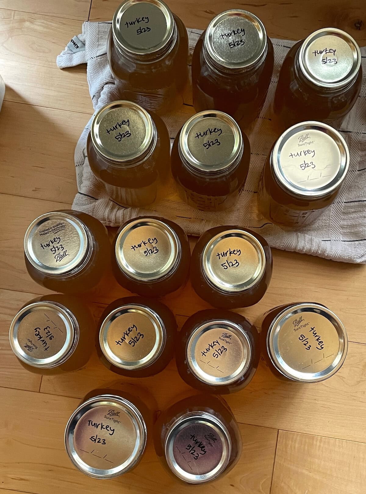 Jars of turkey stock with handwritten labels including dates on a wooden surface.