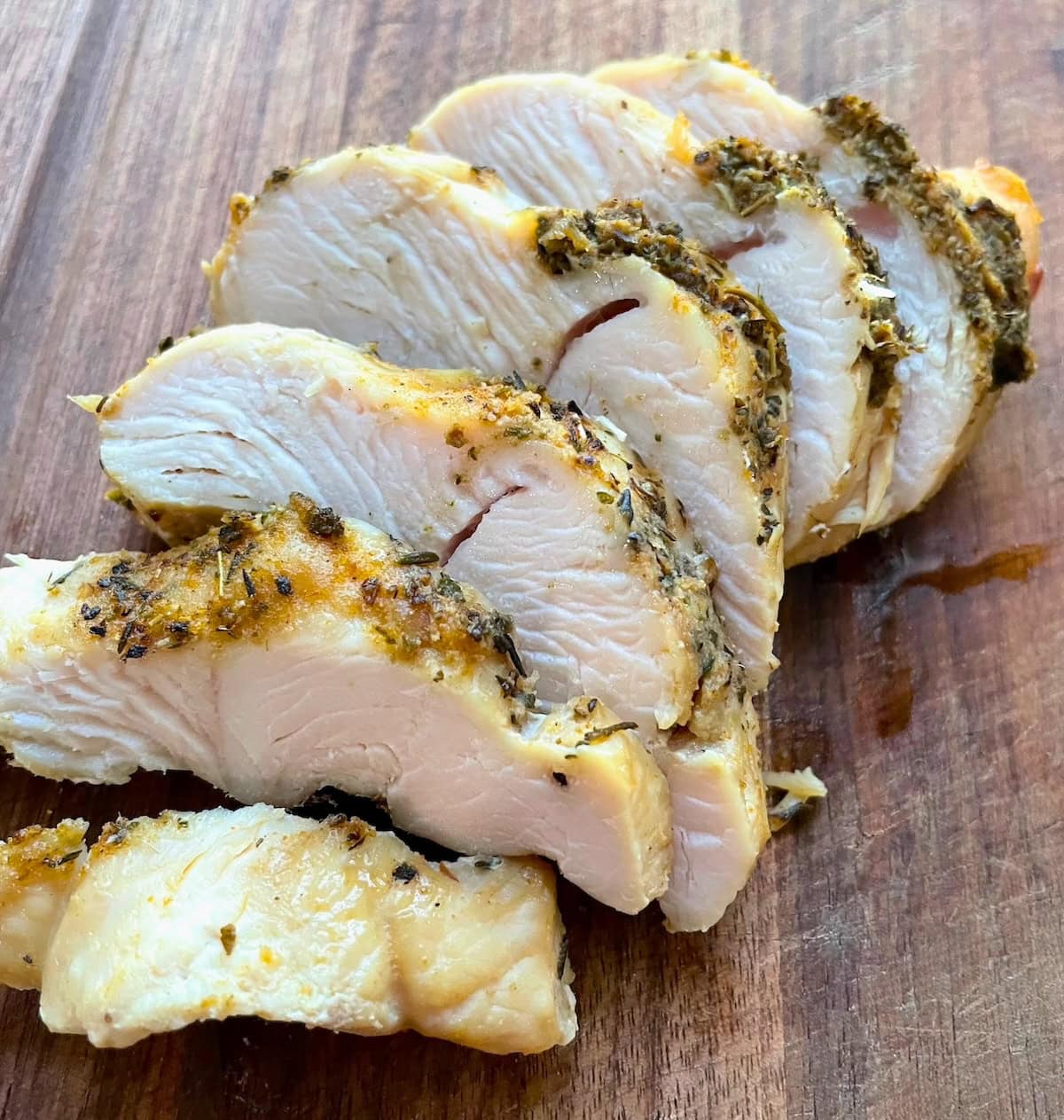 Sliced herb-crusted slow cooked turkey breast on a wooden surface.