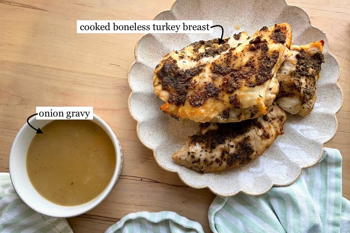 A plate with cooked boneless turkey breast and a bowl of onion gravy on a wooden table.