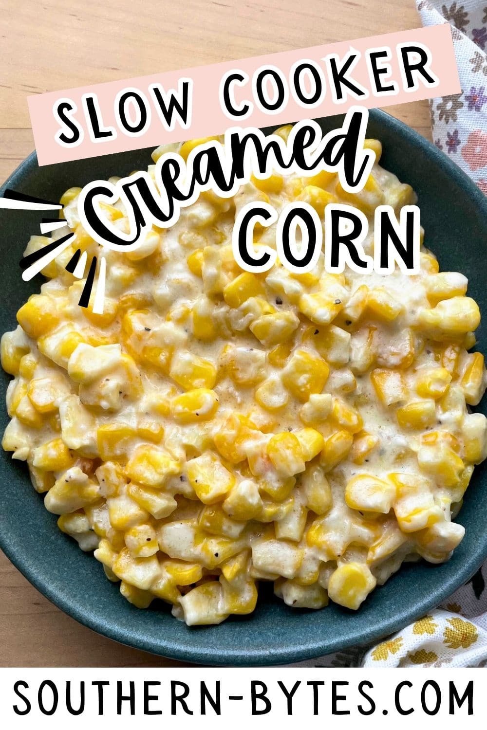 A pin image of a bowl of creamy slow-cooked corn served on a wooden table.