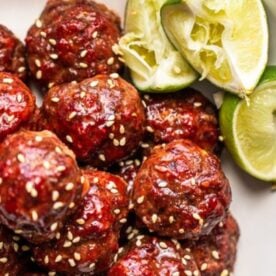 A plate of glazed meatballs sprinkled with sesame seeds, accompanied by lime wedges.