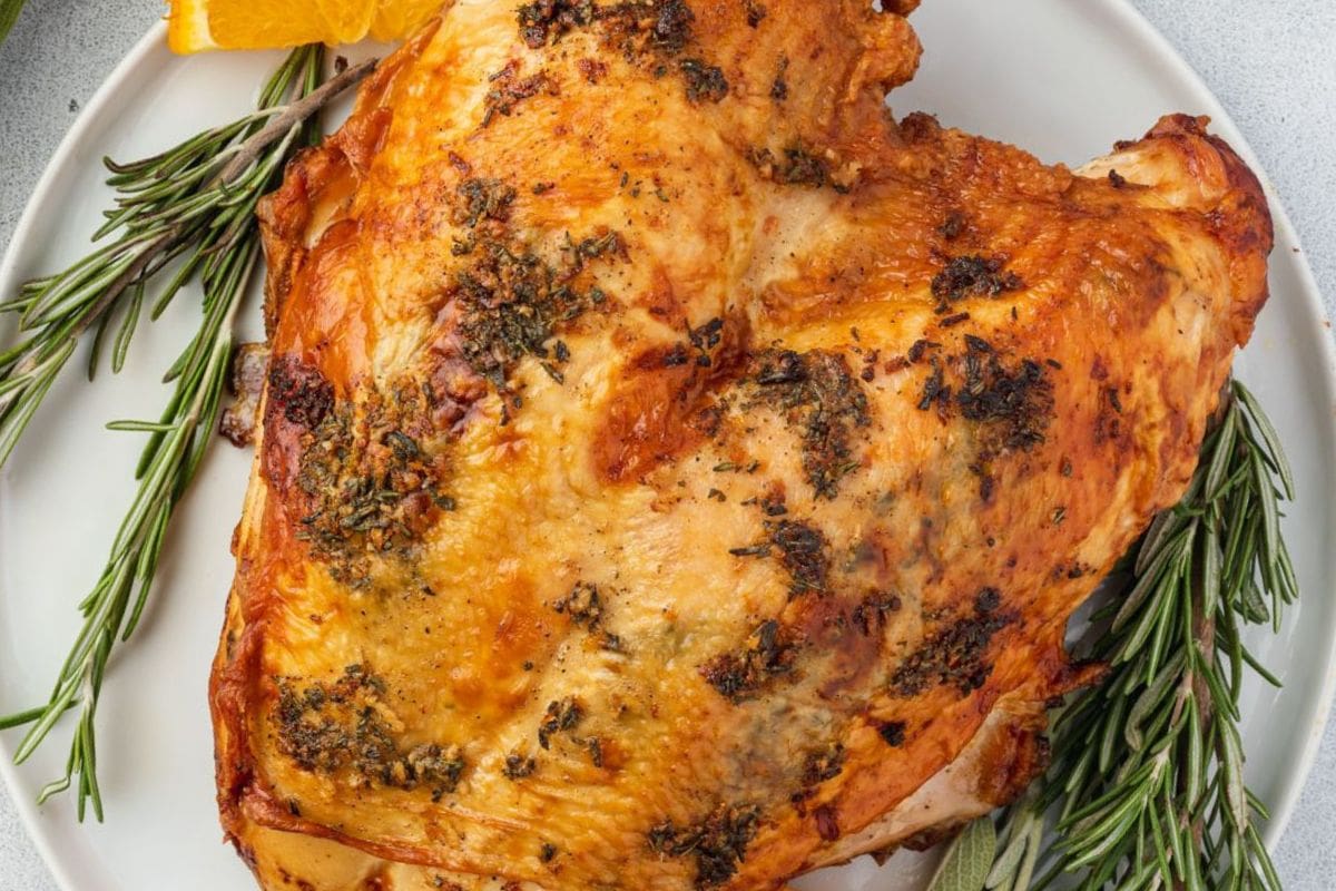 A succulent roasted turkey with herb crust served on a plate with rosemary and orange slices.