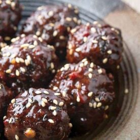 Plate of glazed meatballs sprinkled with sesame seeds.