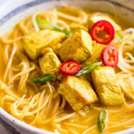 A bowl of spicy chicken noodle soup with sliced red chili and green onions on top.